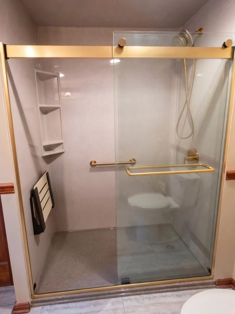 Walk-in shower in brushed gold with flip up seat, detachable wand, safety bars, and a corner caddy