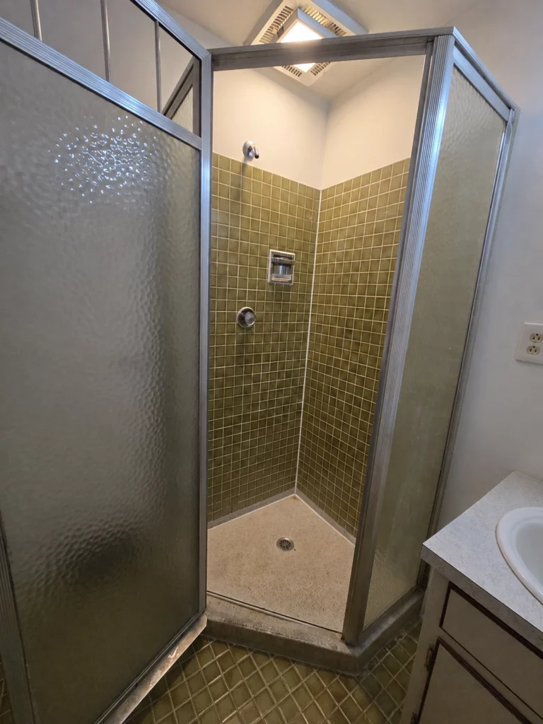An aging corner shower in a small master bathroom before remodeling in Camillus NY